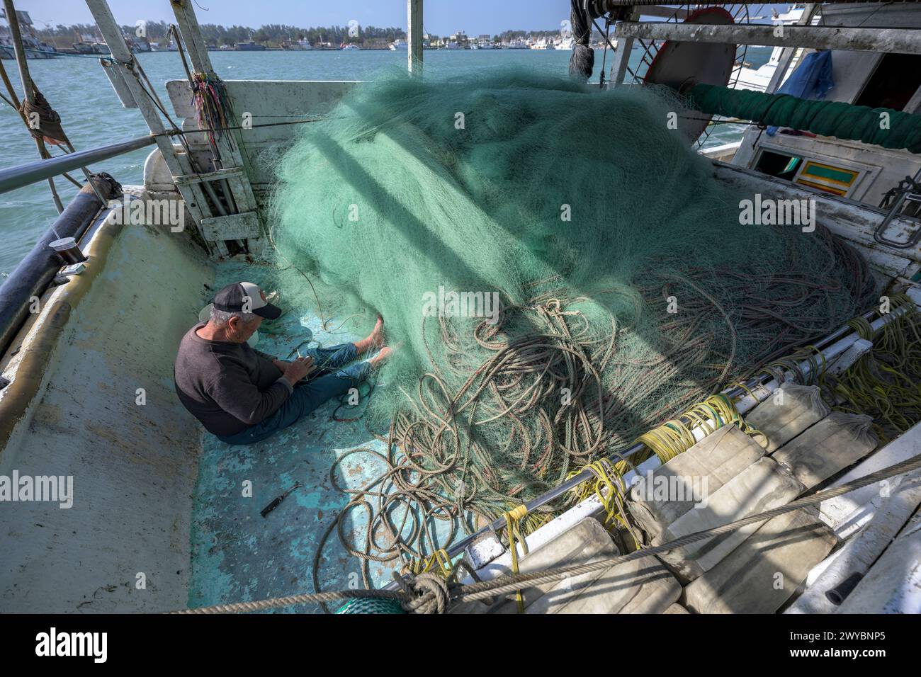Un pescatore ripara diligentemente le reti da pesca su un ponte di barche, mostrando la vita quotidiana del lavoro marittimo Foto Stock