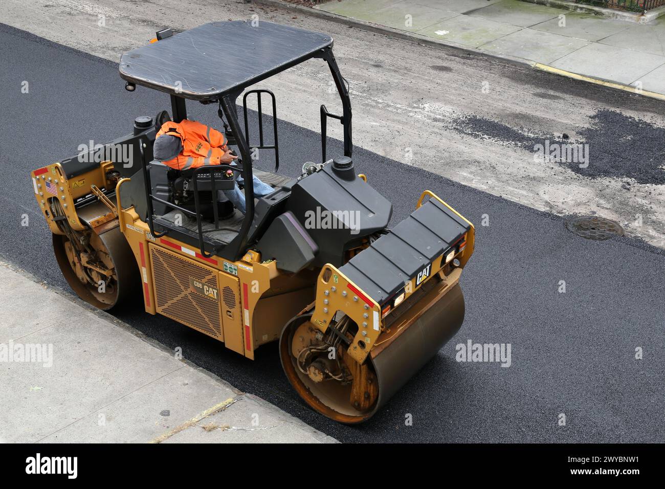 il lavoratore cittadino pavimenta la strada con un veicolo per pavimentazione (nuova installazione di asfalto su strade urbane) rullo vibrante tandem Foto Stock