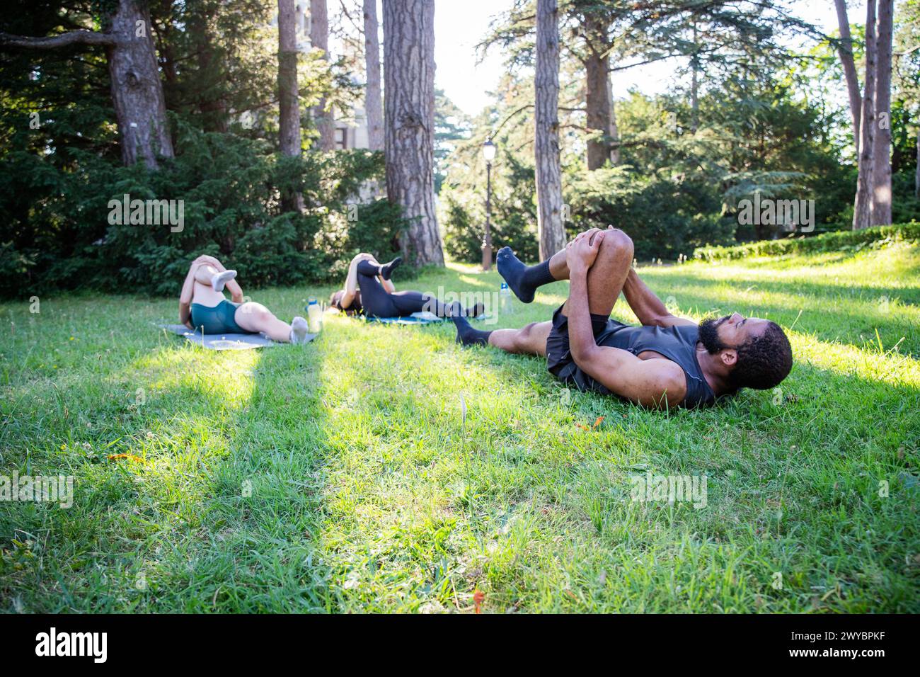 Tre persone stanno sdraiando sull'erba in un parco e si allenano insieme, si adattano allo stile di vita Foto Stock