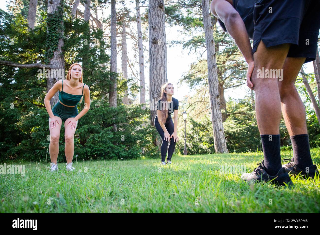 Tre persone sportive si stanno allenando in un parco pubblico, un personal trainer sta tenendo una lezione. Foto Stock