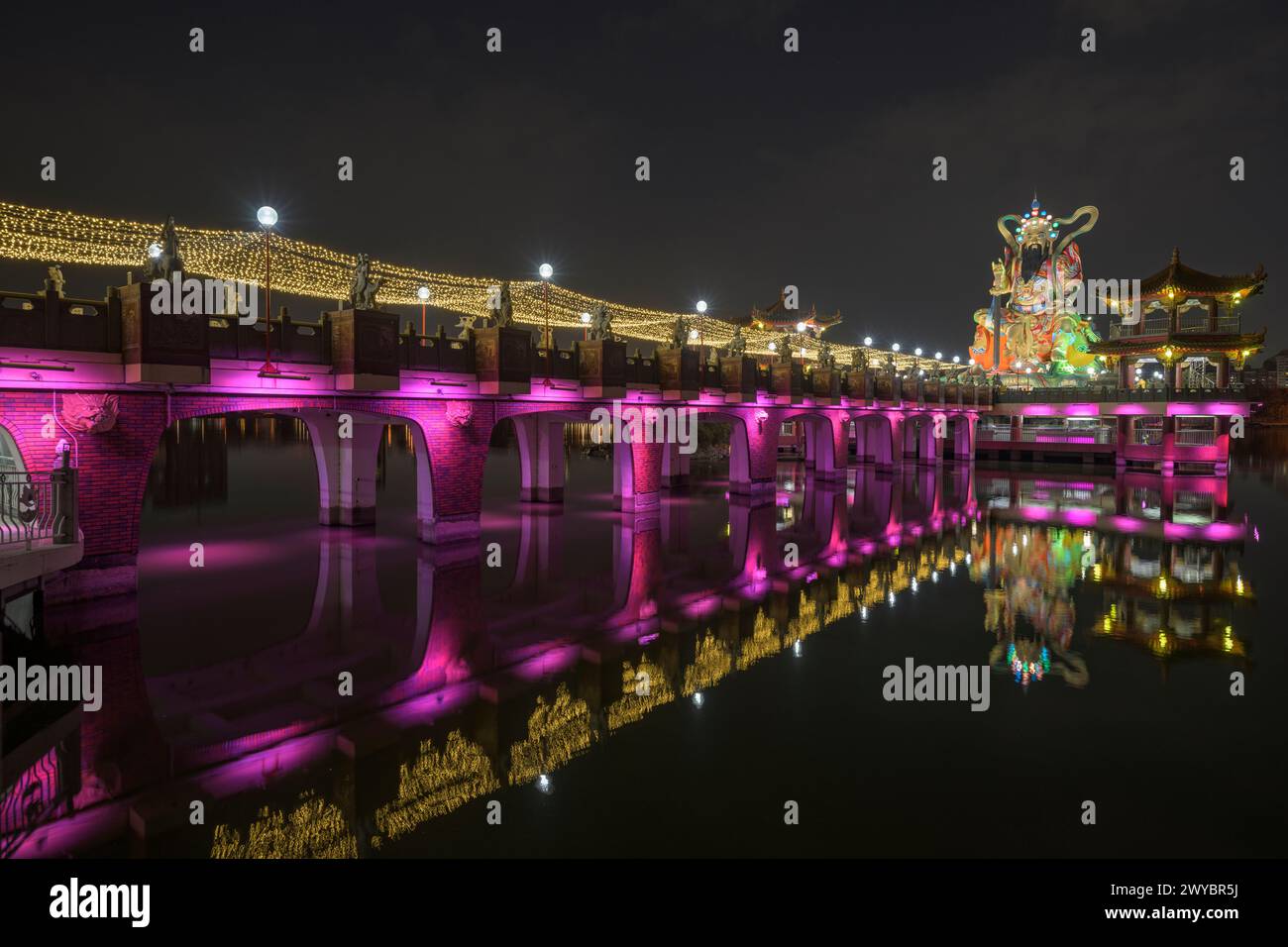 Una foto a lunga esposizione di un ponte del tempio Zuoying Yuandi decorato in modo luminoso e dei suoi riflessi sullo stagno del Loto Zuoying di notte Foto Stock