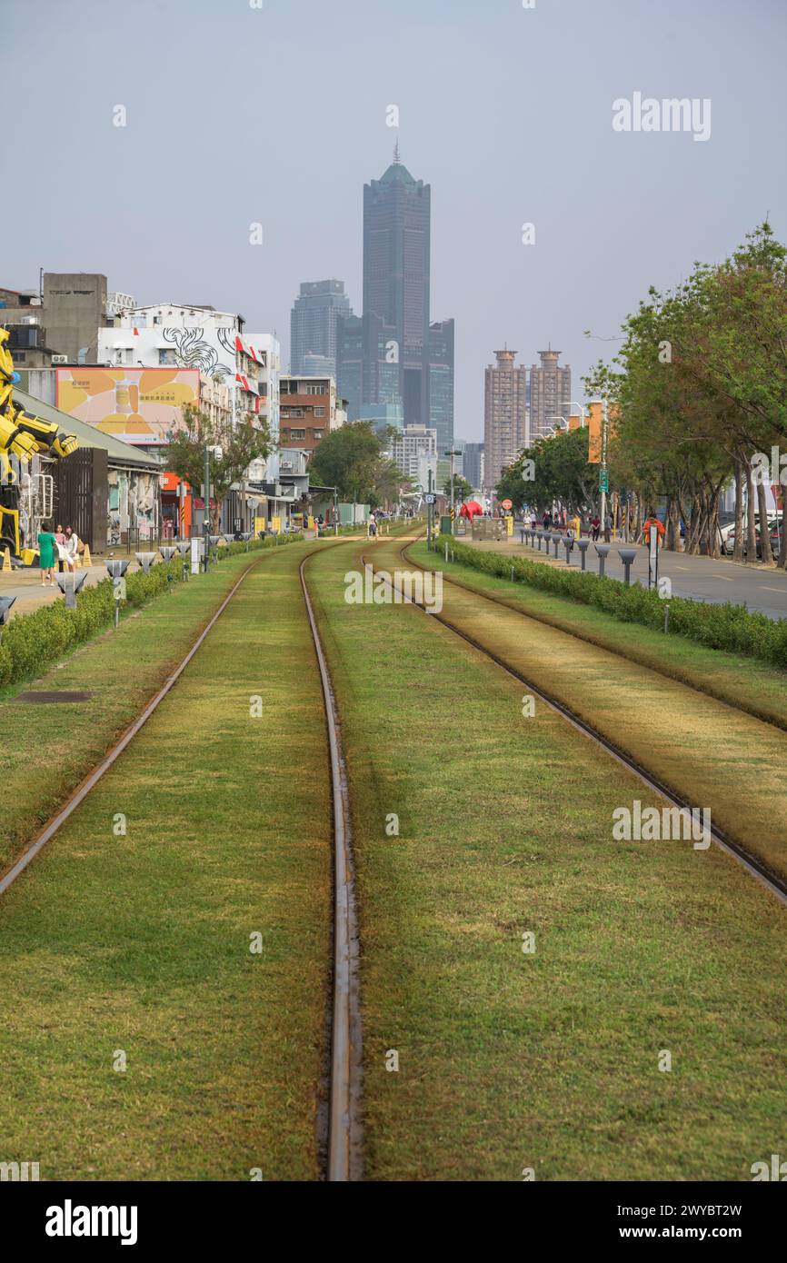 I binari erbosi della ferrovia conducono a un torreggiante skyline della città in una miscela di elementi industriali e naturali Foto Stock