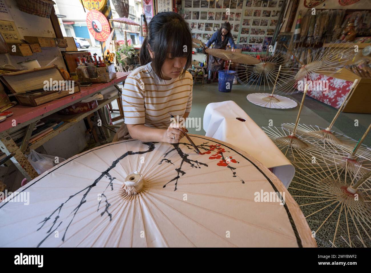 In un laboratorio, un artista decora un ombrello di carta con intricati disegni floreali Foto Stock