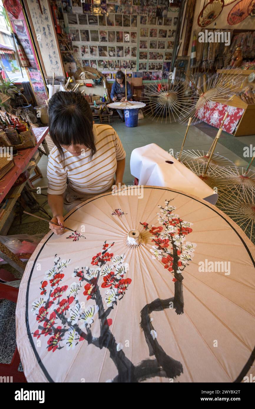 In un laboratorio, un artista decora un ombrello di carta con intricati disegni floreali Foto Stock