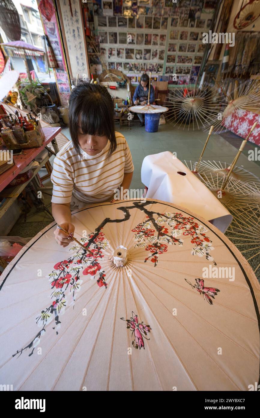 In un laboratorio, un artista decora un ombrello di carta con intricati disegni floreali Foto Stock
