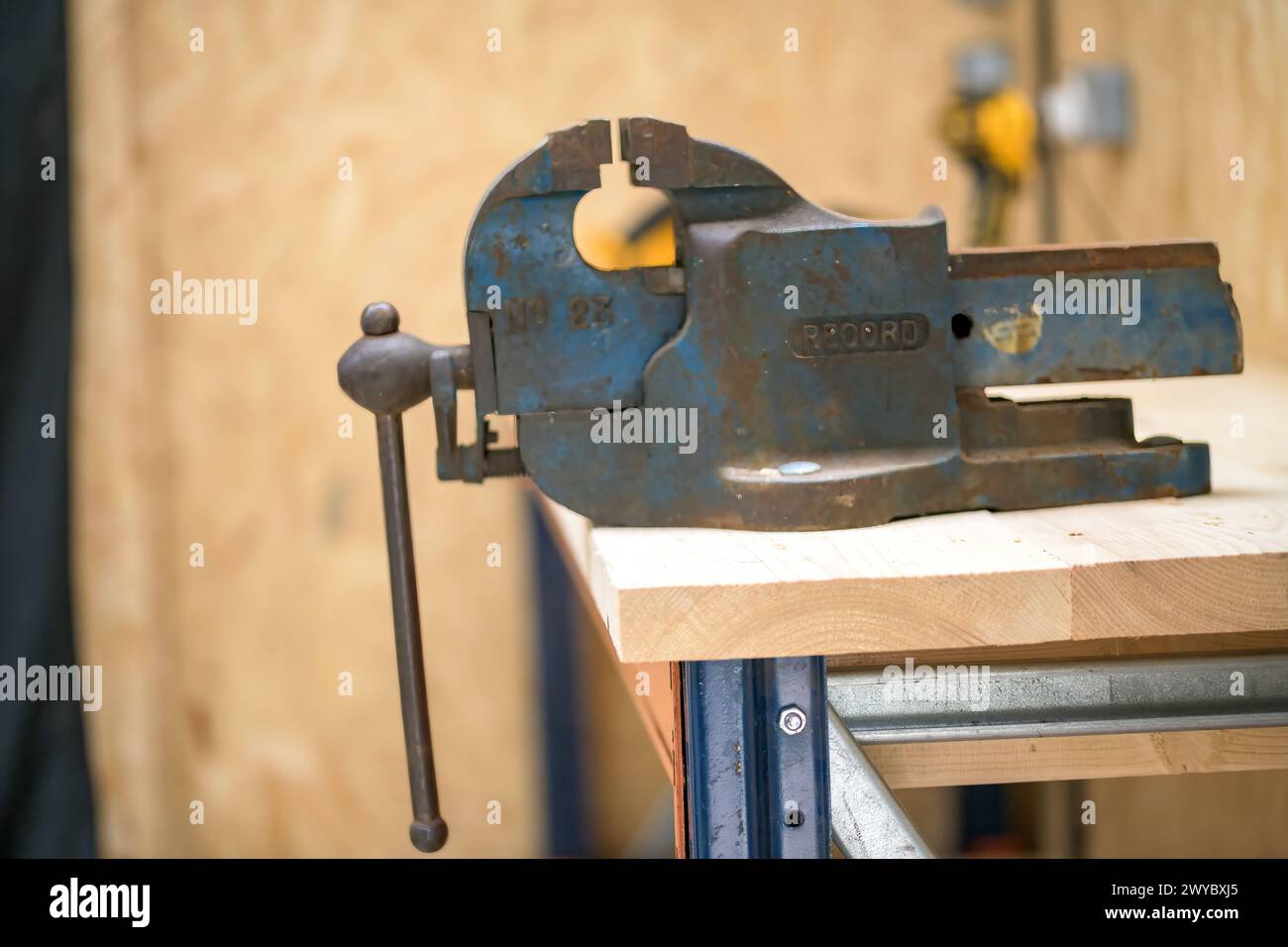 Una morsa da banco obsoleta, posizionata su un piano di lavoro di nuova formazione costituito da ponteggi e piedistallo in metallo Foto Stock