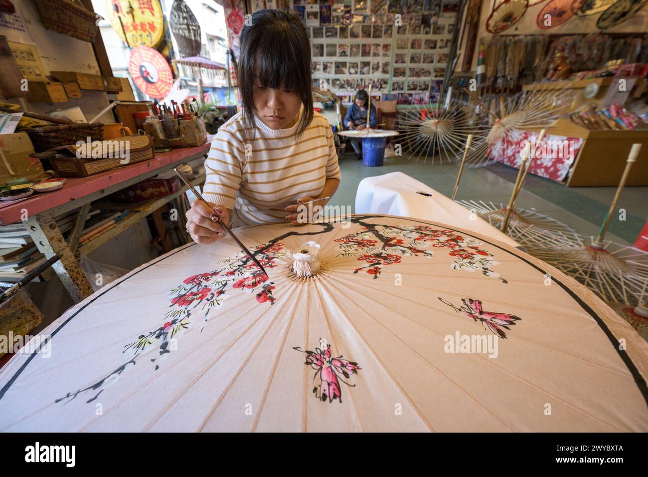 In un laboratorio, un artista decora un ombrello di carta con intricati disegni floreali Foto Stock