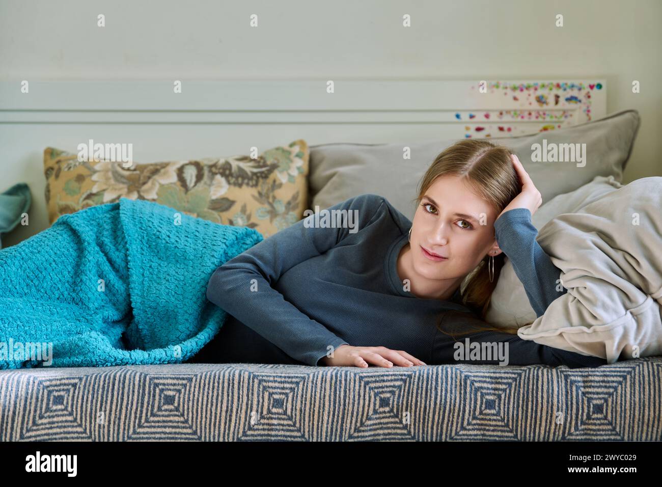 Bella giovane donna che si rilassa sotto la coperta a casa, guardando la macchina fotografica Foto Stock