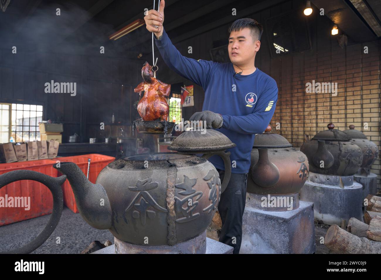 Un uomo che cucina un pollo usando tradizionali vasi di argilla sopra un fuoco a legna Foto Stock