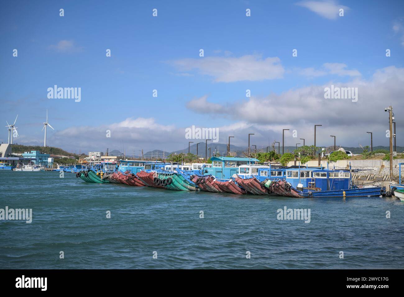 Barche da pesca blu ormeggiate in un porto con acque calme e turbine eoliche sullo sfondo Foto Stock