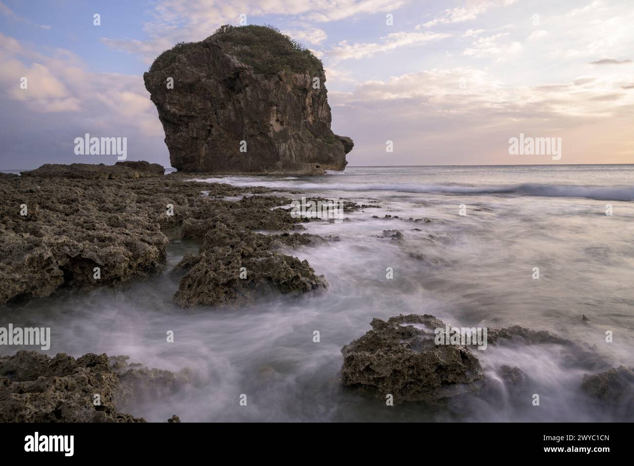 Un tramonto sereno con un affioramento roccioso alto in mezzo a un mare setoso con un effetto di lunga esposizione Foto Stock
