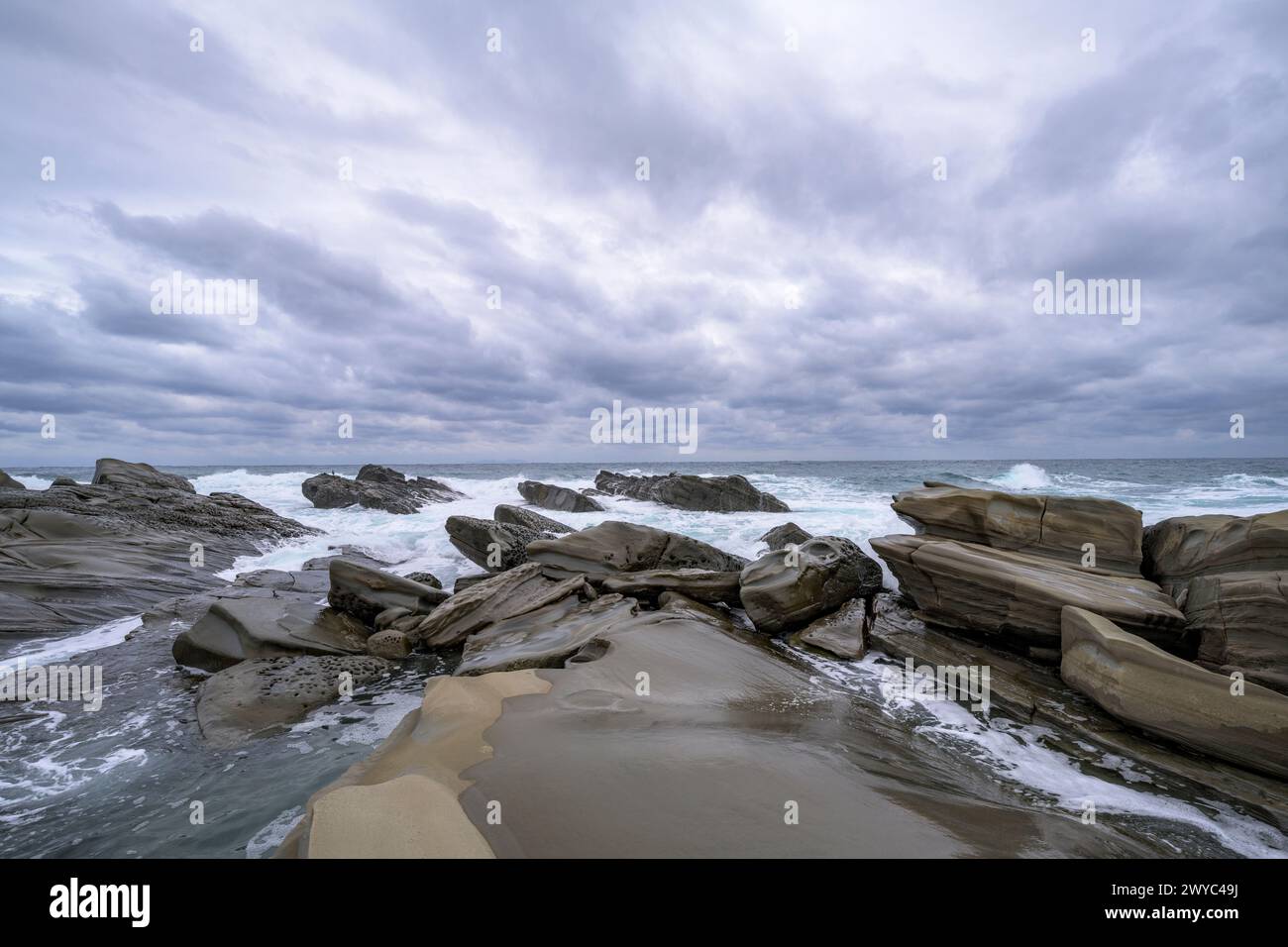 Accattivanti formazioni rocciose sullo sfondo di potenti onde marine dalle cime bianche sotto un cielo tempestoso Foto Stock