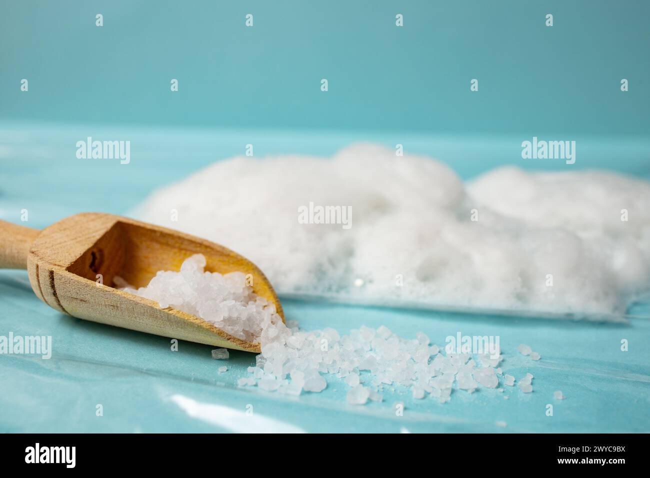 Sgrossare il sale in una paletta in legno accanto al gommoso bianco su sfondo blu, con messa a fuoco morbida Foto Stock