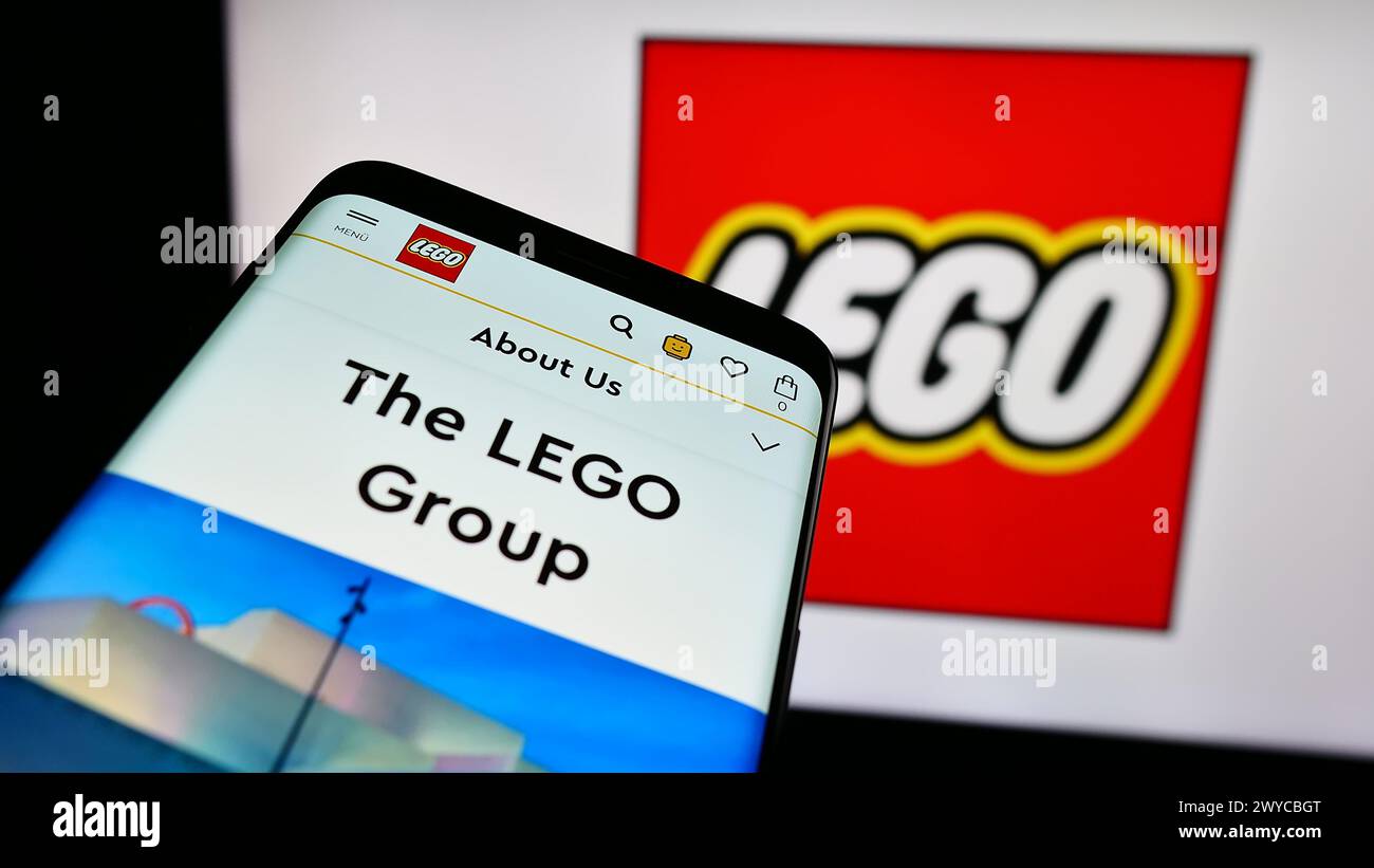 Smartphone con sito web della società danese LEGO di giocattoli da costruzione davanti al logo aziendale. Mettere a fuoco in alto a sinistra sul display del telefono. Foto Stock
