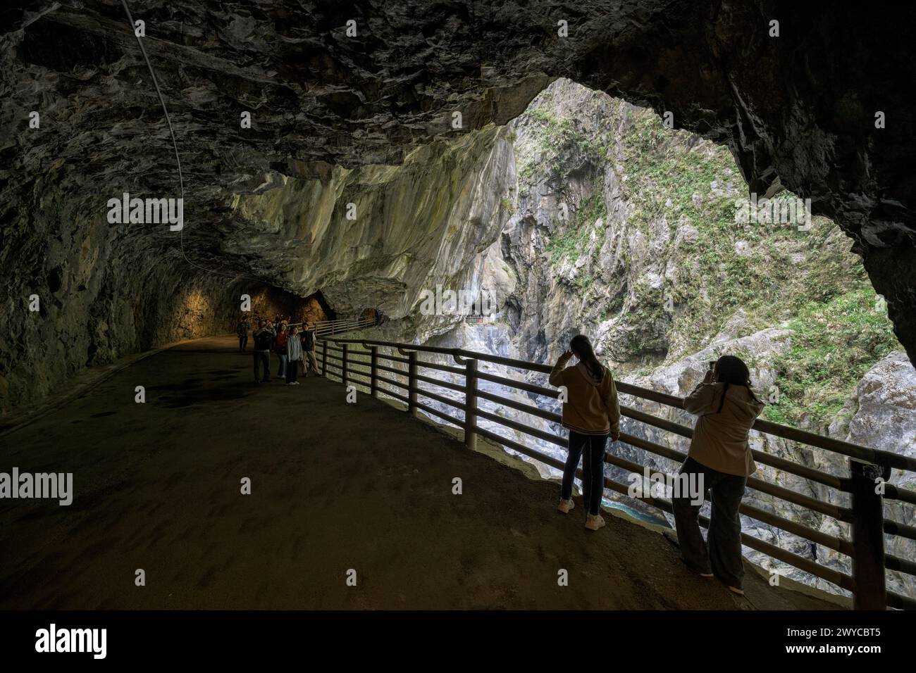 I turisti si radunano lungo un sentiero recintato all'interno di un tunnel di grotta ammirando la splendida gola di Taroko all'esterno Foto Stock