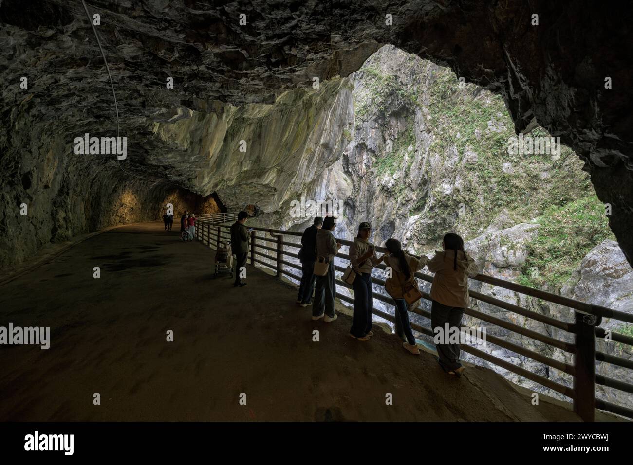 I turisti si radunano lungo un sentiero recintato all'interno di un tunnel di grotta ammirando la splendida gola di Taroko all'esterno Foto Stock