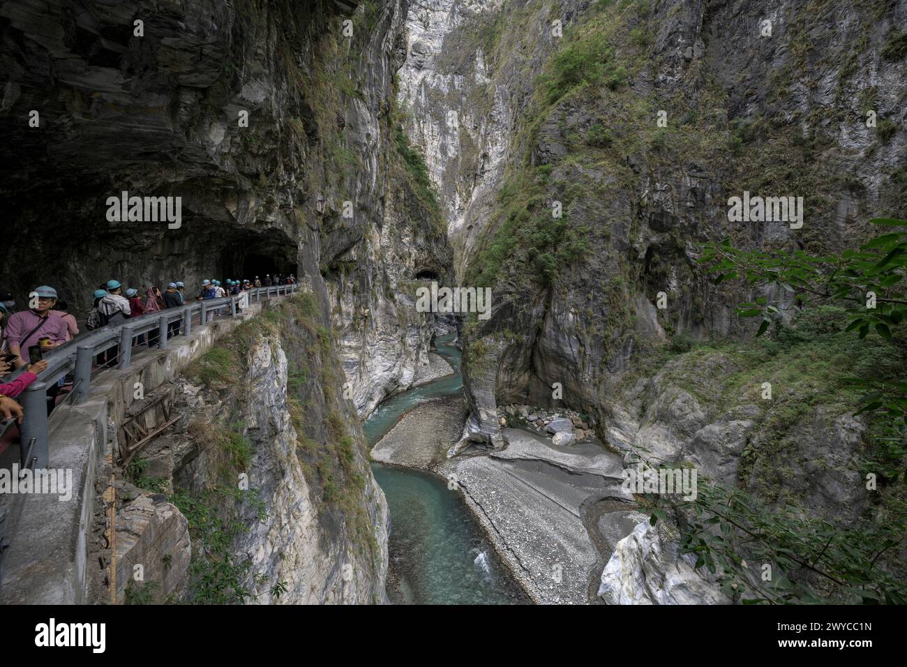 I turisti si radunano lungo un sentiero recintato all'interno di un tunnel di grotta ammirando la splendida gola di Taroko all'esterno Foto Stock