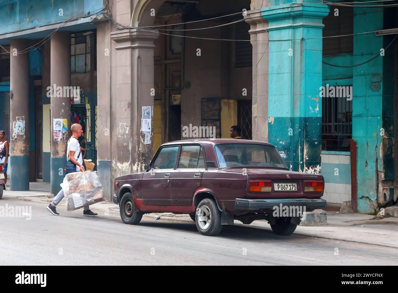 Uomo cubano che cammina in macchina Lada, facciata di edifici intemprati, a l'Avana, Cuba Foto Stock