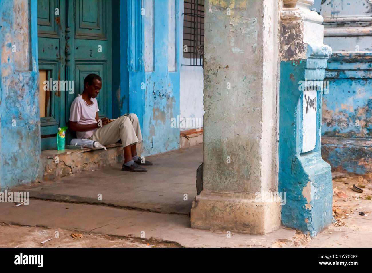 Un uomo cubano snello seduto davanti alla porta di una porta rotta a l'Avana, Cuba Foto Stock