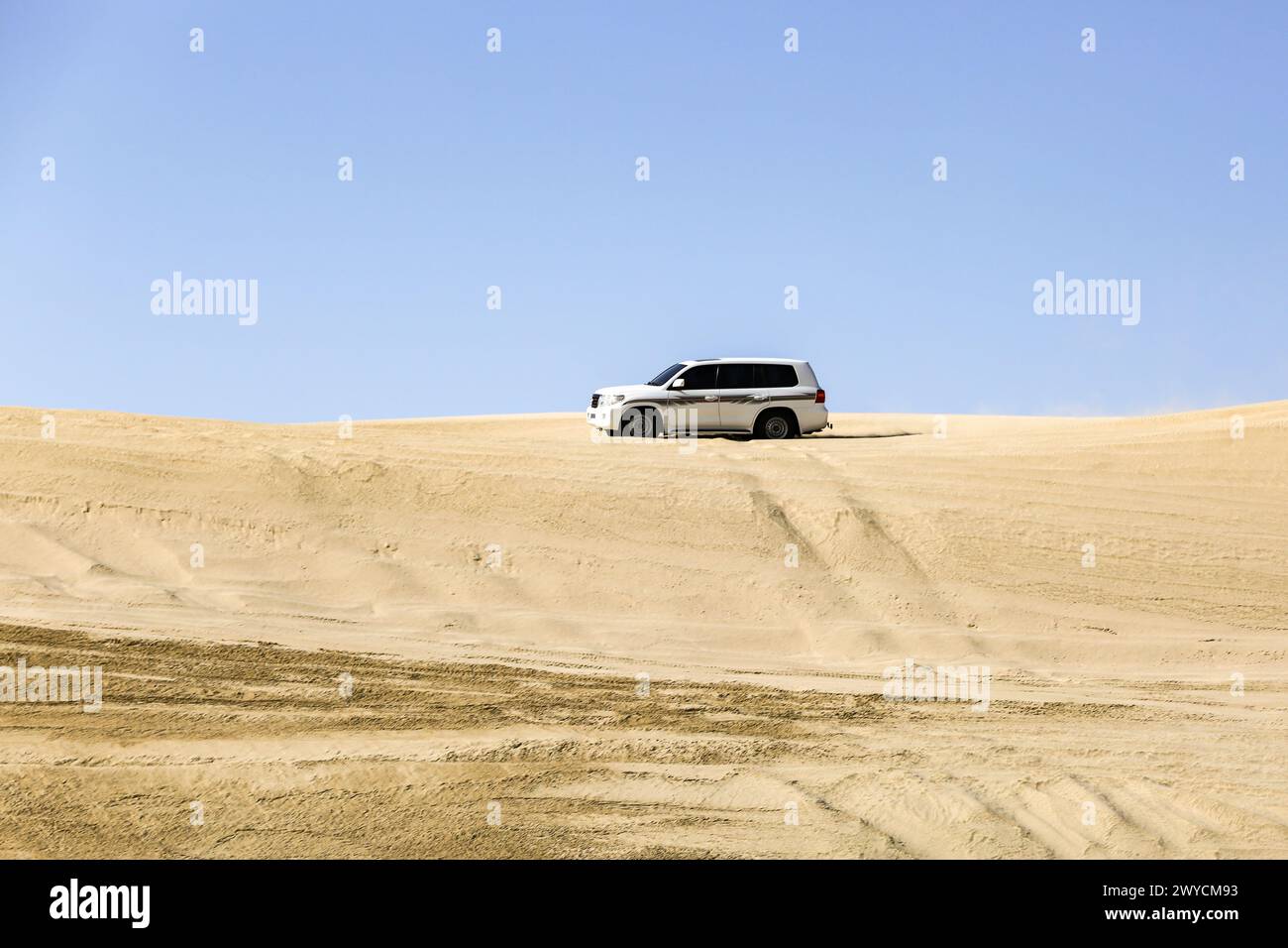 Una grande auto bianca fuoristrada che trasporta i turisti attraverso le attraenti dune di sabbia nel deserto del Qatar. Foto Stock