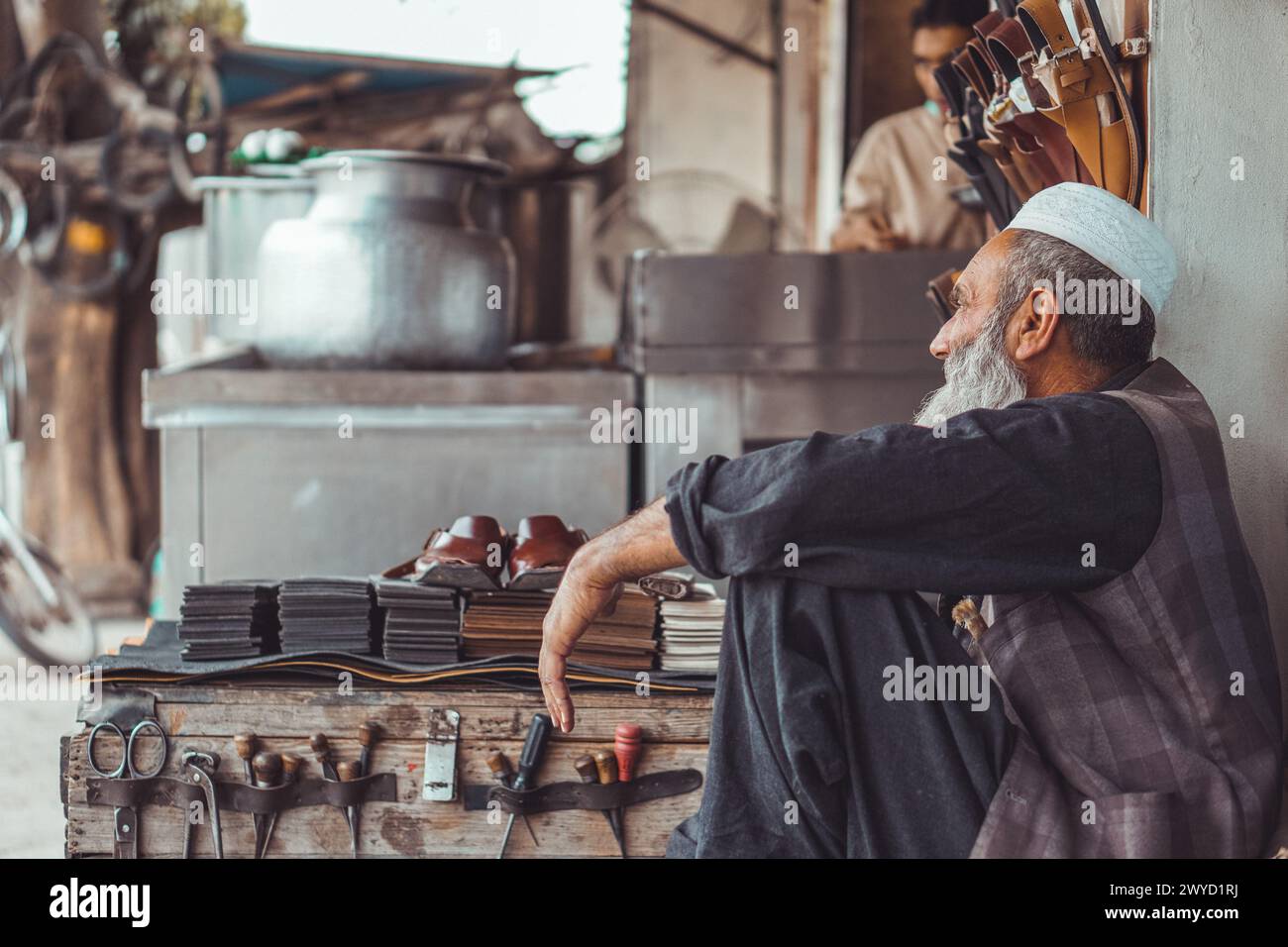 Povero vecchio pakistano Pathan calzolaio per le strade locali del Pakistan con le sue scarpe in pelle fatte a mano e gli attrezzi di riparazione nel suo negozio di strada Foto Stock