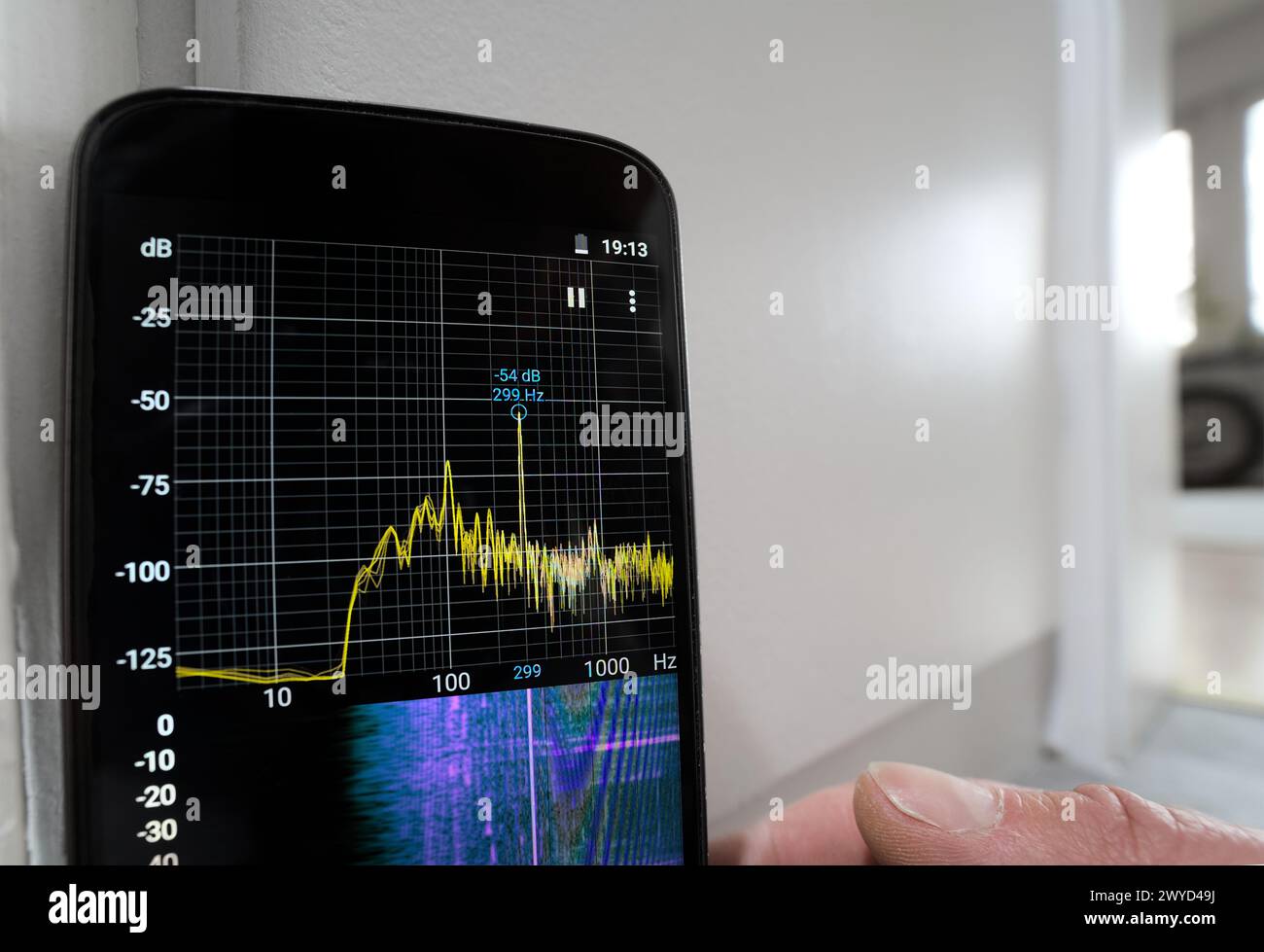 Persona con misuratore del livello di rumore sonoro alla ricerca di un guasto per inquinamento parassita della frequenza del ronzio con l'impianto elettrico interno della banda dell'app per smartphone Foto Stock