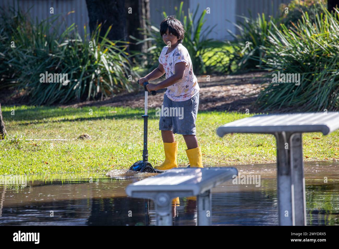 Sabato 6 aprile 2024. Sydney è stata colpita da un diluvio di pioggia nelle ultime 48 ore, con alcune aree, tra cui Penrith, che hanno ricevuto le piogge più pesanti di sempre, a Narrabeen i residenti intorno alla laguna di Narabeen, nella foto, sono stati invitati ad evacuare a causa dell'innalzamento del livello dell'acqua dal lago Narrabeen sulle spiagge settentrionali di Sydney. dove sono caduti oltre 150 mm di pioggia. Ci sono stati oltre 50 avvistamenti di inondazioni lungo i fiumi nel nuovo Galles del Sud e si prevede che la diga di Warragamba fuoriesca. Il ragazzo con stivali gialli gioca sul suo scooter nell'acqua piena. Accreditate le notizie dal vivo di Martin Berry @alamy. Foto Stock