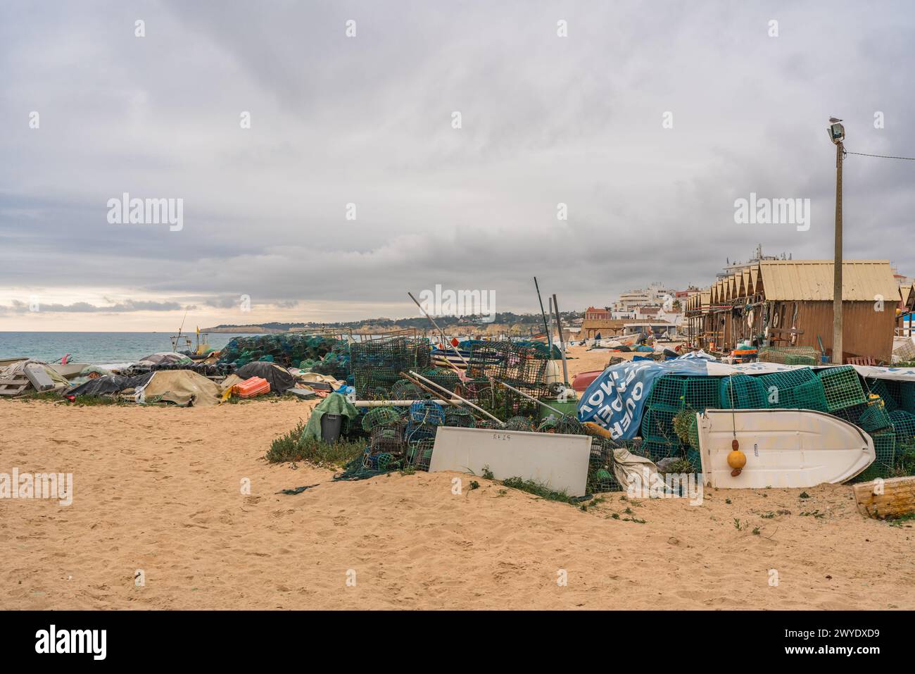 Attrezzatura da pesca e barche sparse su una spiaggia sabbiosa sotto un cielo nuvoloso. Foto Stock