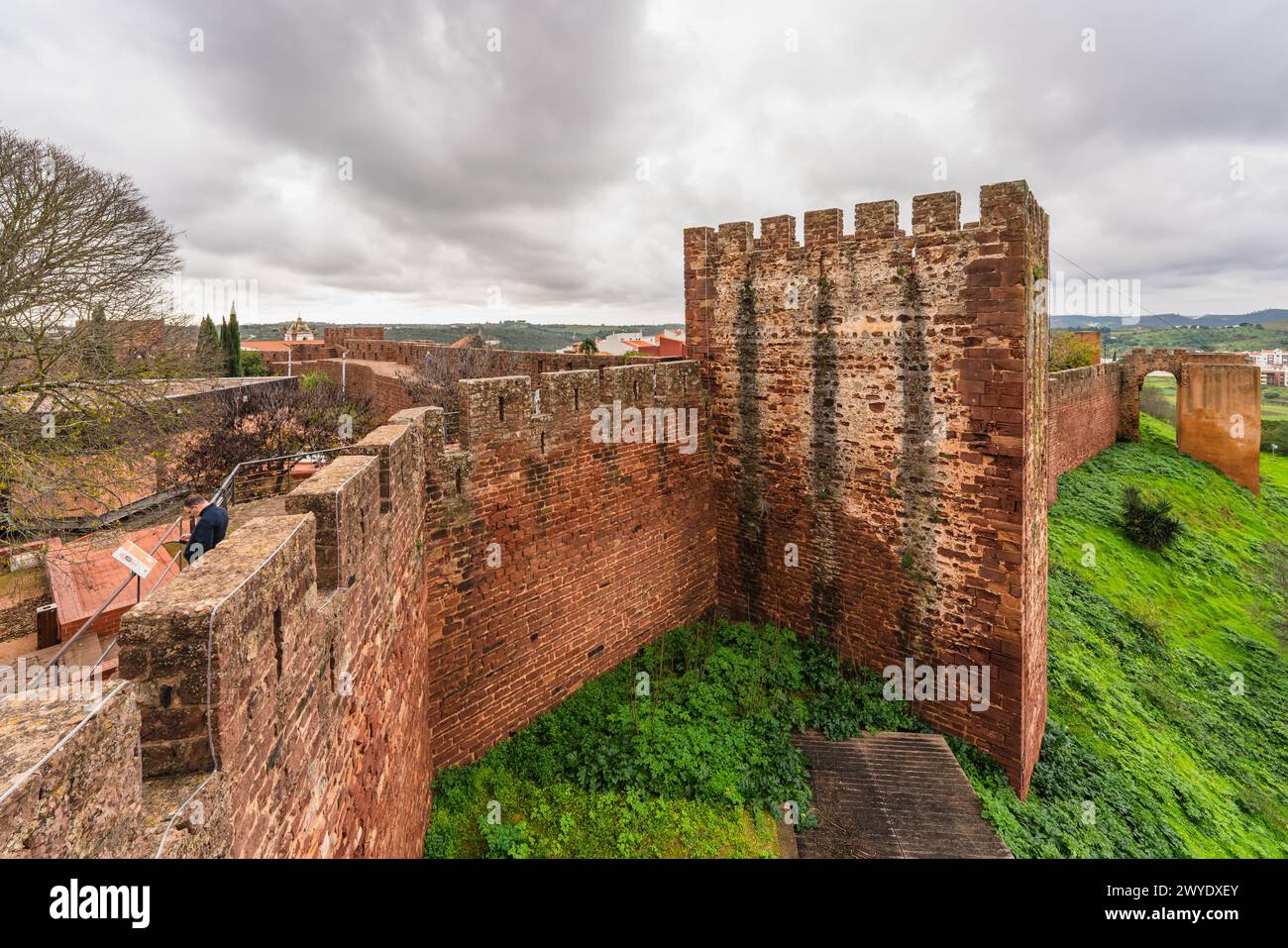 Le robuste mura rosse del Castello di Silves, con un visitatore che si gode la vista dai bastioni. Foto Stock