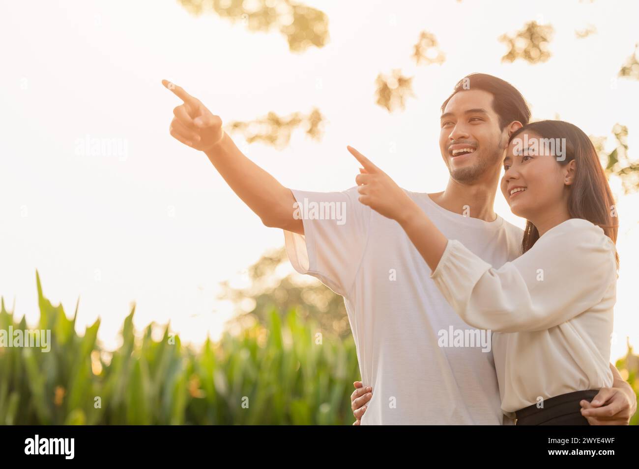 coppia adolescente in piedi felice sorridere insieme parco all'aperto sole che splende mano puntando in alto per la pianificazione della vita futuro concetto di visione aziendale assicurativa Foto Stock
