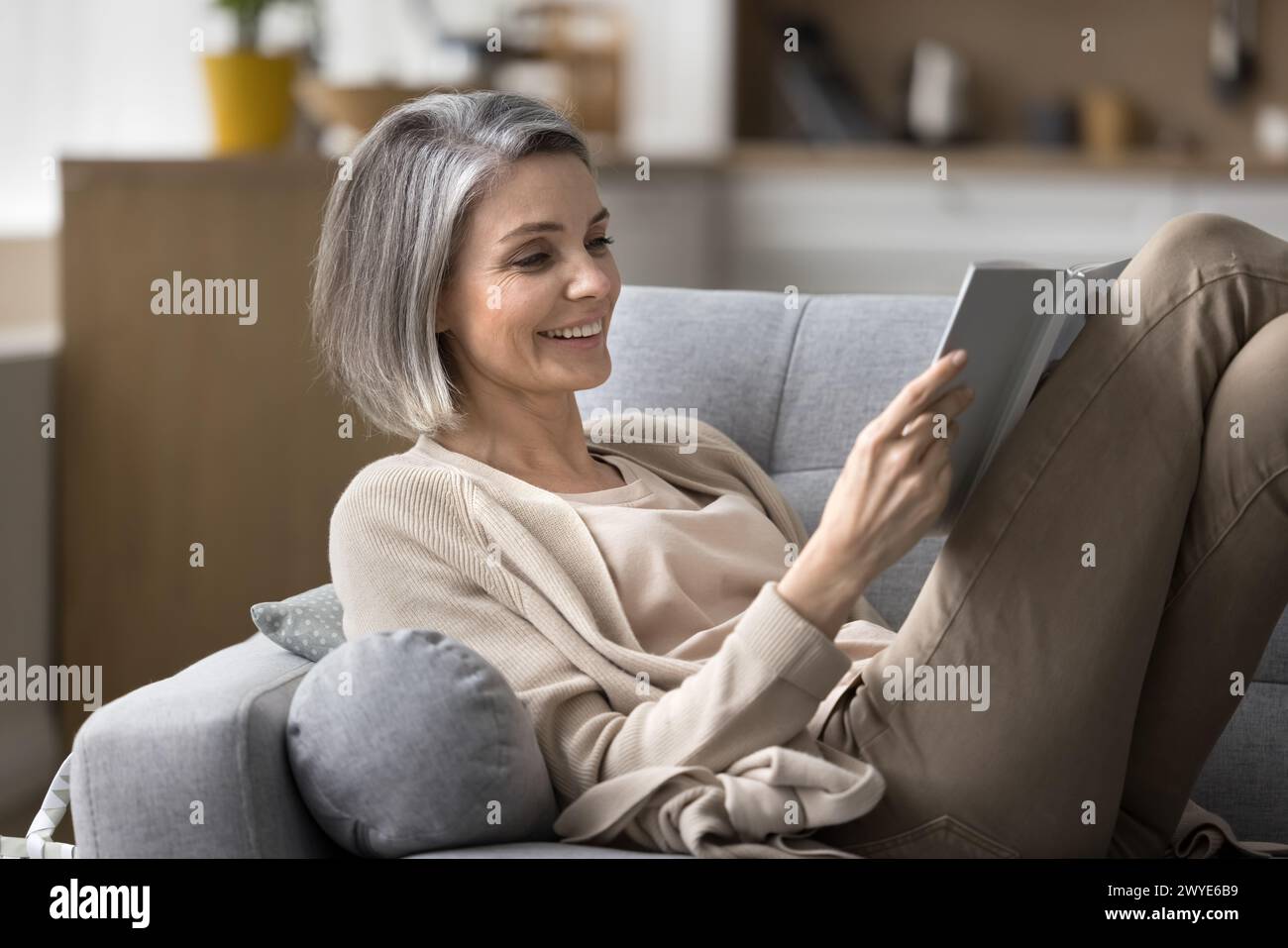Una donna matura sorridente leggeva un libro rilassante sul divano a casa Foto Stock