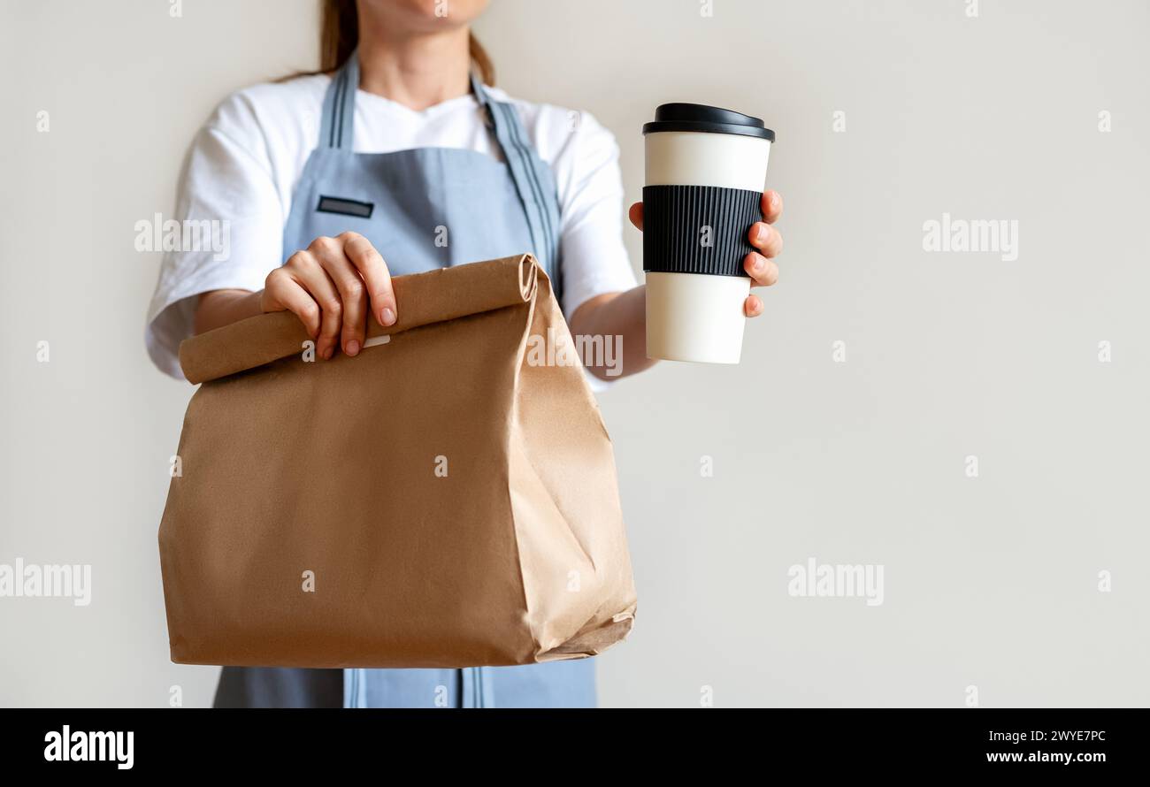 Concetto di cibo da asporto. La cameriera dava al cliente una tazza di caffè e un sacchetto di carta con il pasto. Foto Stock