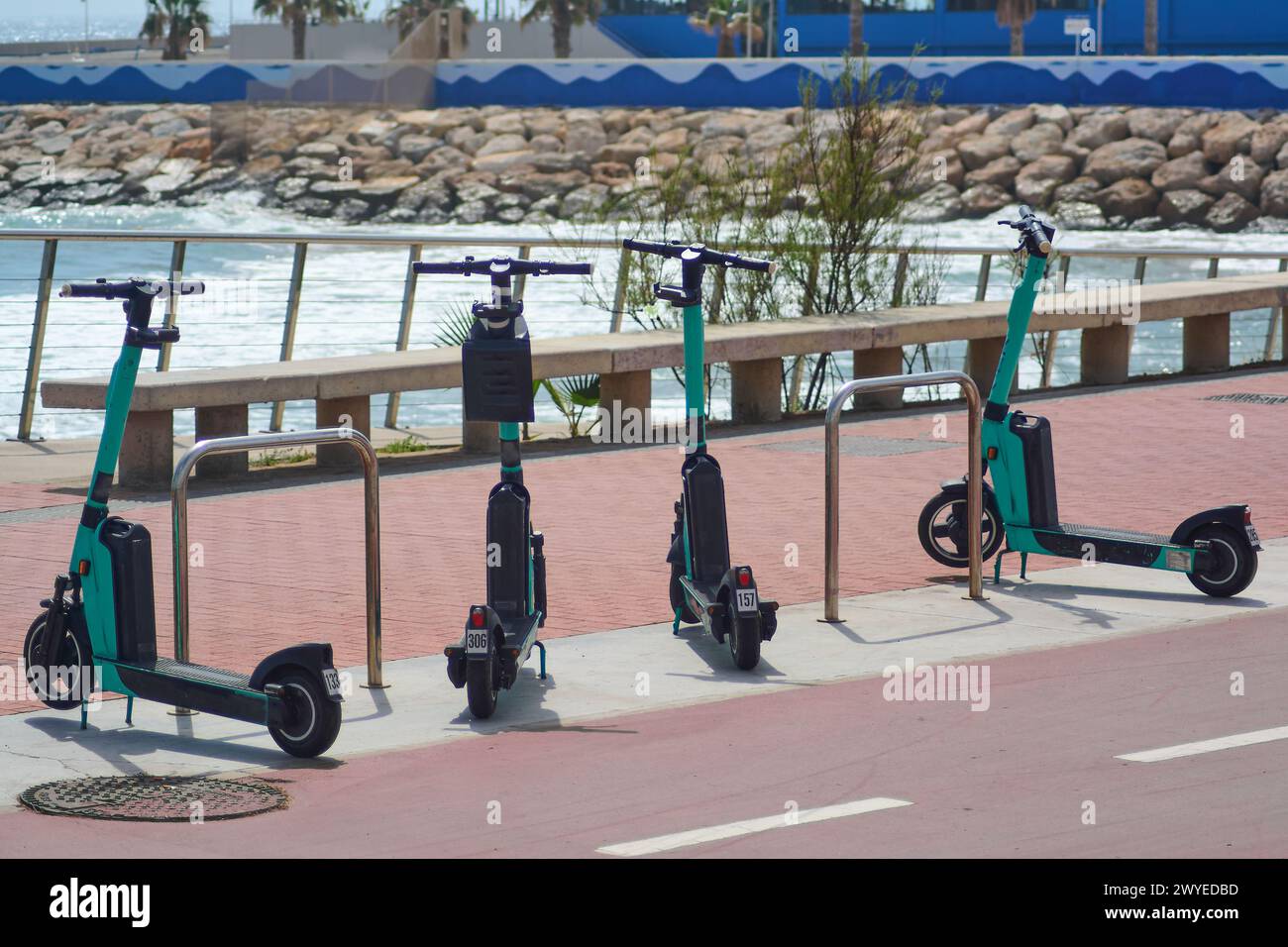 Tre scooter elettrici parcheggiati lungo la ringhiera di una passerella, con l'oceano e le rocce sullo sfondo, pronti per essere noleggiati ed esplorare la costa Foto Stock