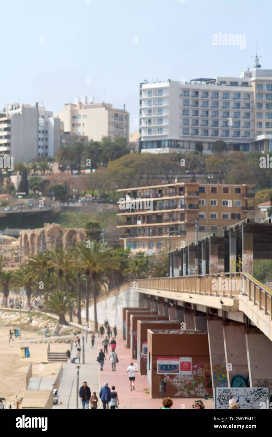 Tarragona, Spagna - 6 aprile 2024: L'immagine mostra la tranquillità della spiaggia di Tarragona con visitatori sparsi, architettura urbana e palme, refle Foto Stock