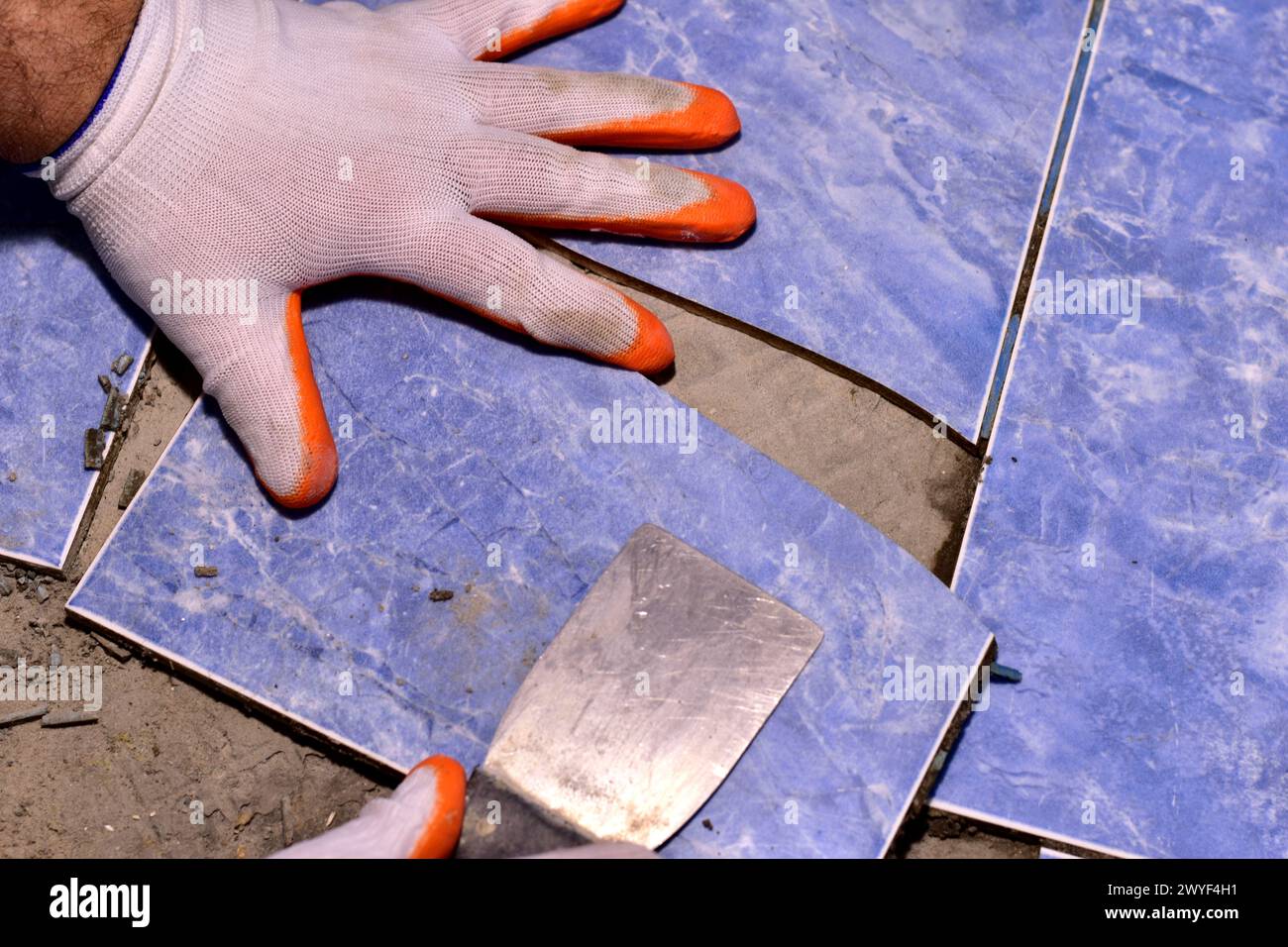 Il padrone con una spatola strappa le piastrelle di ceramica incrinate dal pavimento del bagno. Foto Stock