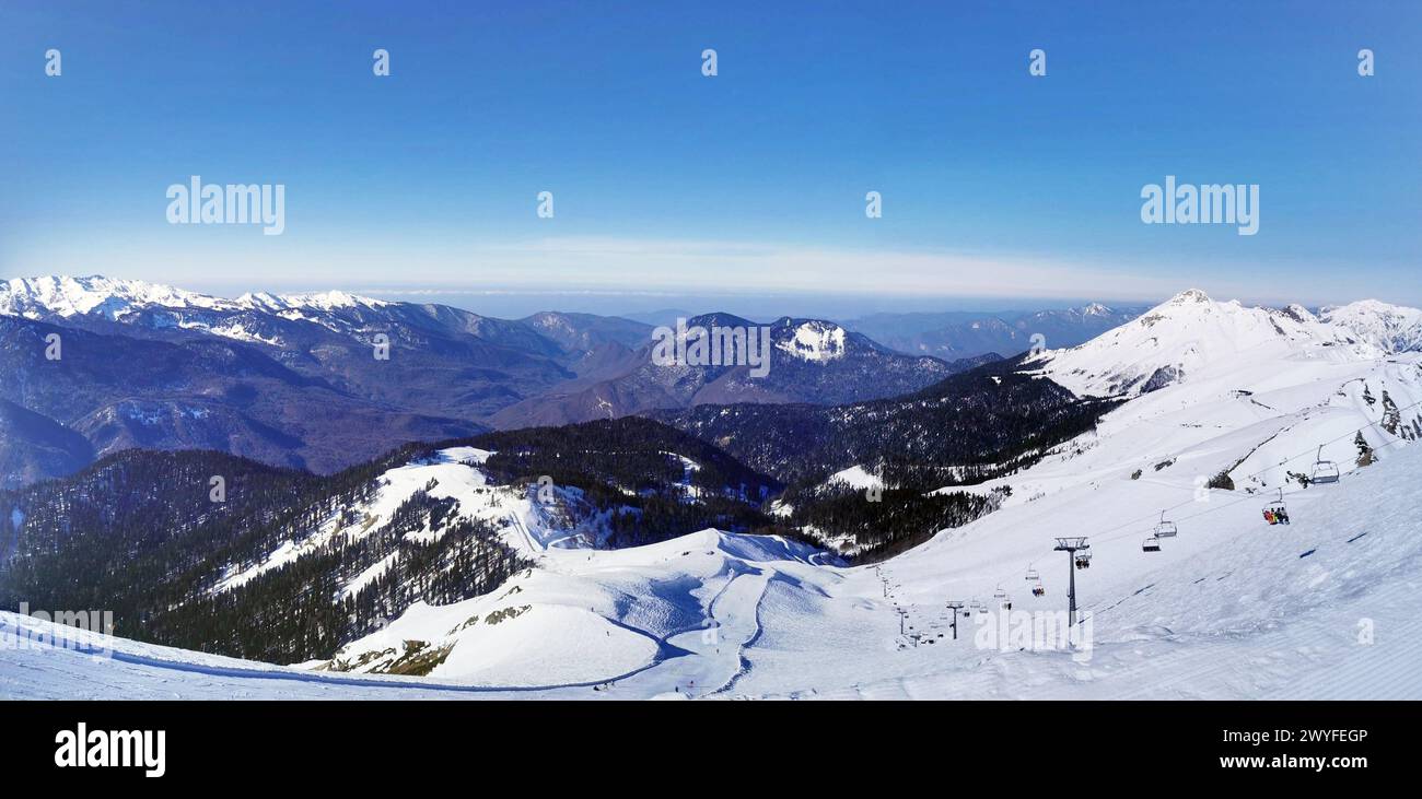 Ampia vista panoramica di una catena montuosa innevata sotto un cielo azzurro. Foto Stock