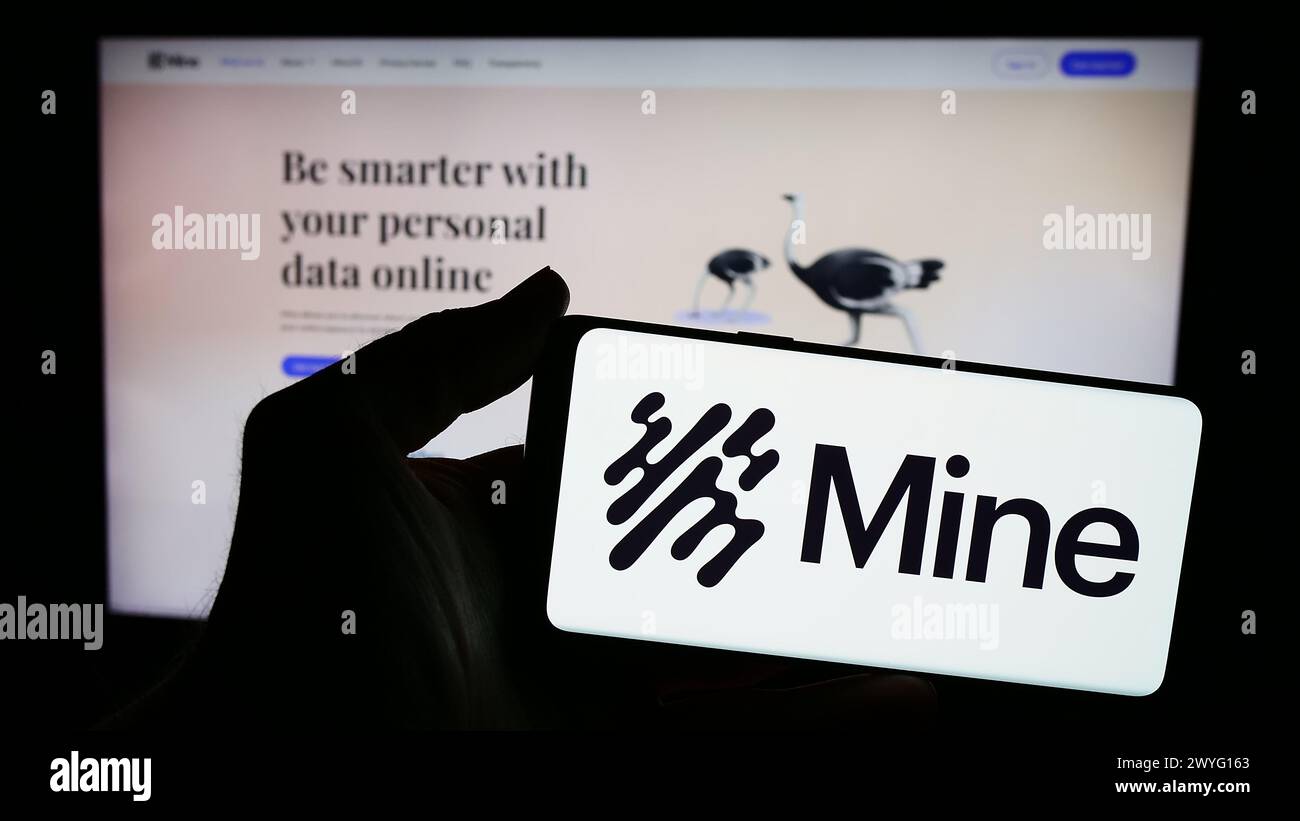 Persona che possiede uno smartphone con il logo della società del sistema operativo Saymine Technologies Ltd. (Mio) di fronte al sito web. Mettere a fuoco il display del telefono. Foto Stock