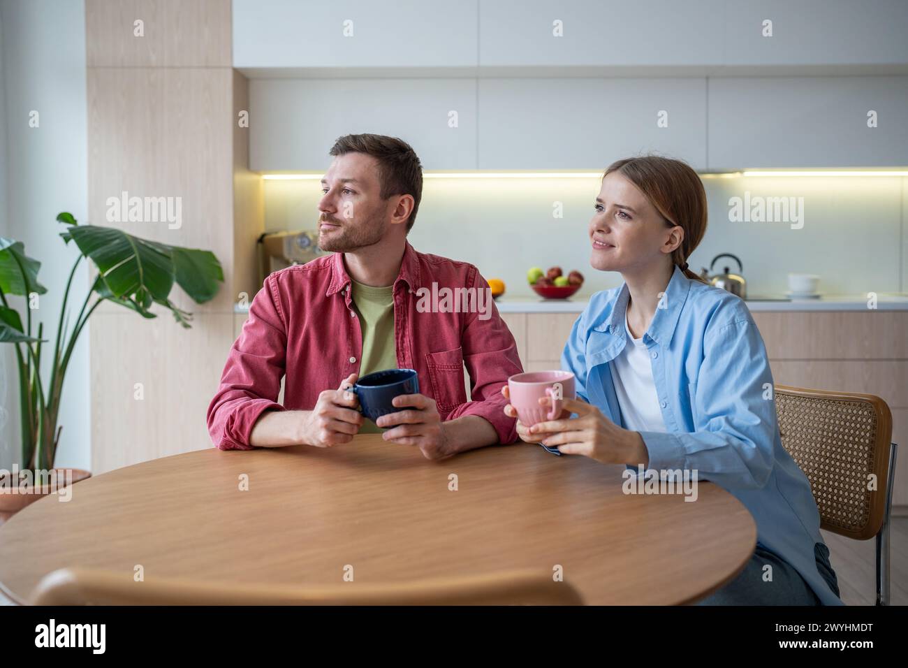 Un uomo e una donna felici si siedono in cucina con una tazza di tè, e guardano con attenzione a sognare un futuro luminoso. Foto Stock