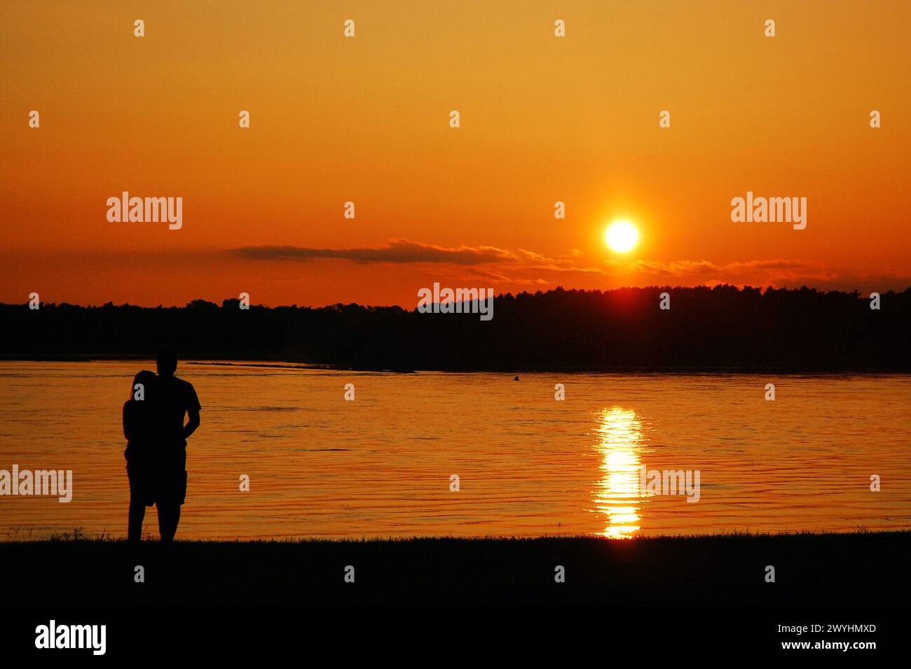 Una giovane coppia adulta si gode la vista del sole che tramonta sul fiume Mississippi vicino a Memphis, mentre il tramonto li rende in forma Foto Stock
