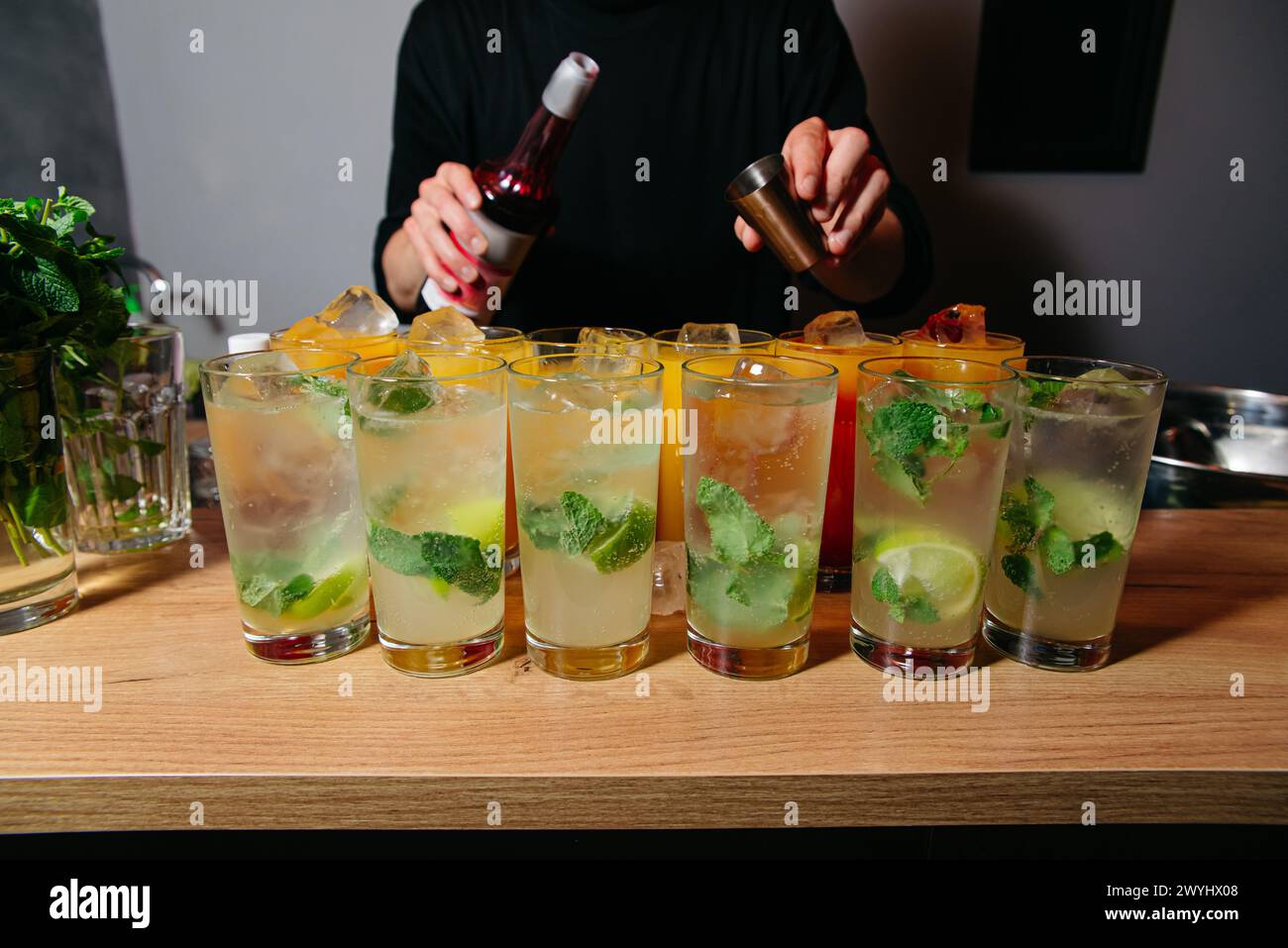 Una gamma di cocktail mojito preparati con menta fresca, lime e ghiaccio su un bancone bar in legno da un barista. Foto Stock