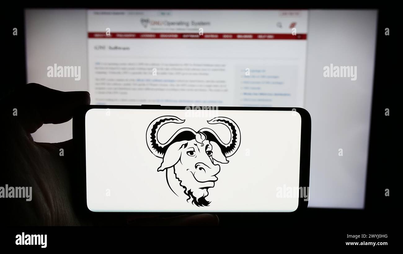 Persona che detiene un cellulare con il logo del progetto di collaborazione software progetto GNU davanti alla pagina web. Mettere a fuoco il display del telefono. Foto Stock