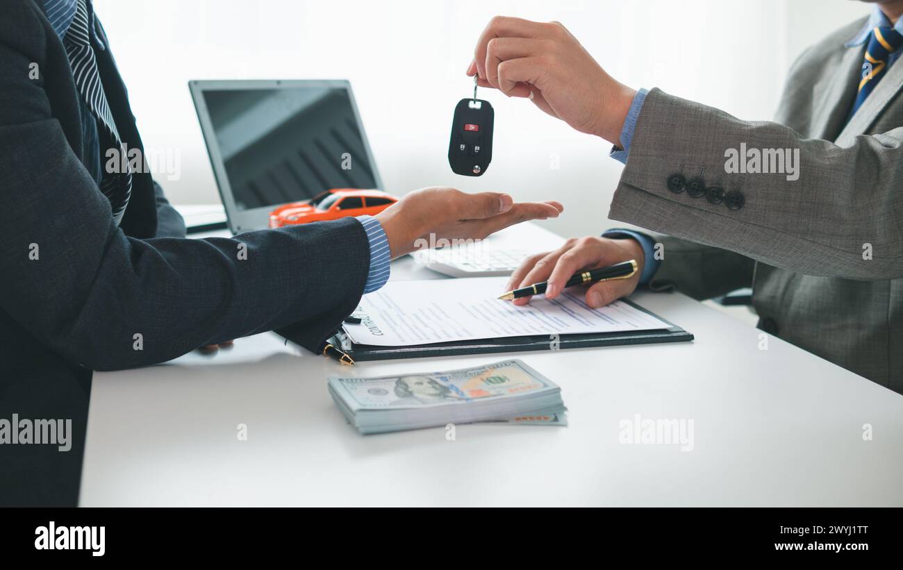 il concessionario sta consegnando le chiavi al cliente dopo la firma del contratto di vendita e del contratto rateale. Concetto di consegna delle chiavi dell'auto a cu Foto Stock