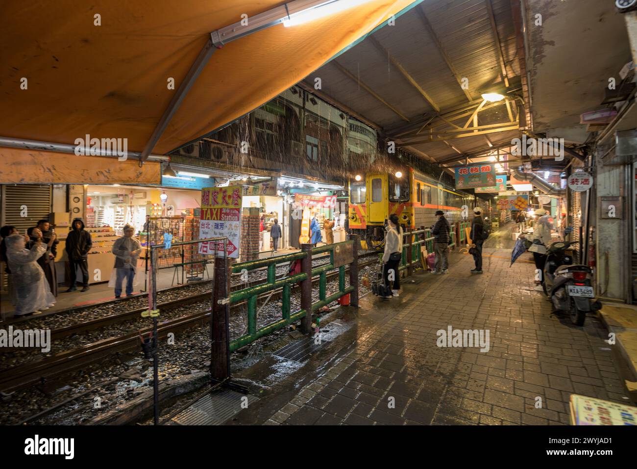 Treno notturno che passa per le strette strade di Shifen mentre i passanti scattano foto e aspettano di attraversare i binari Foto Stock