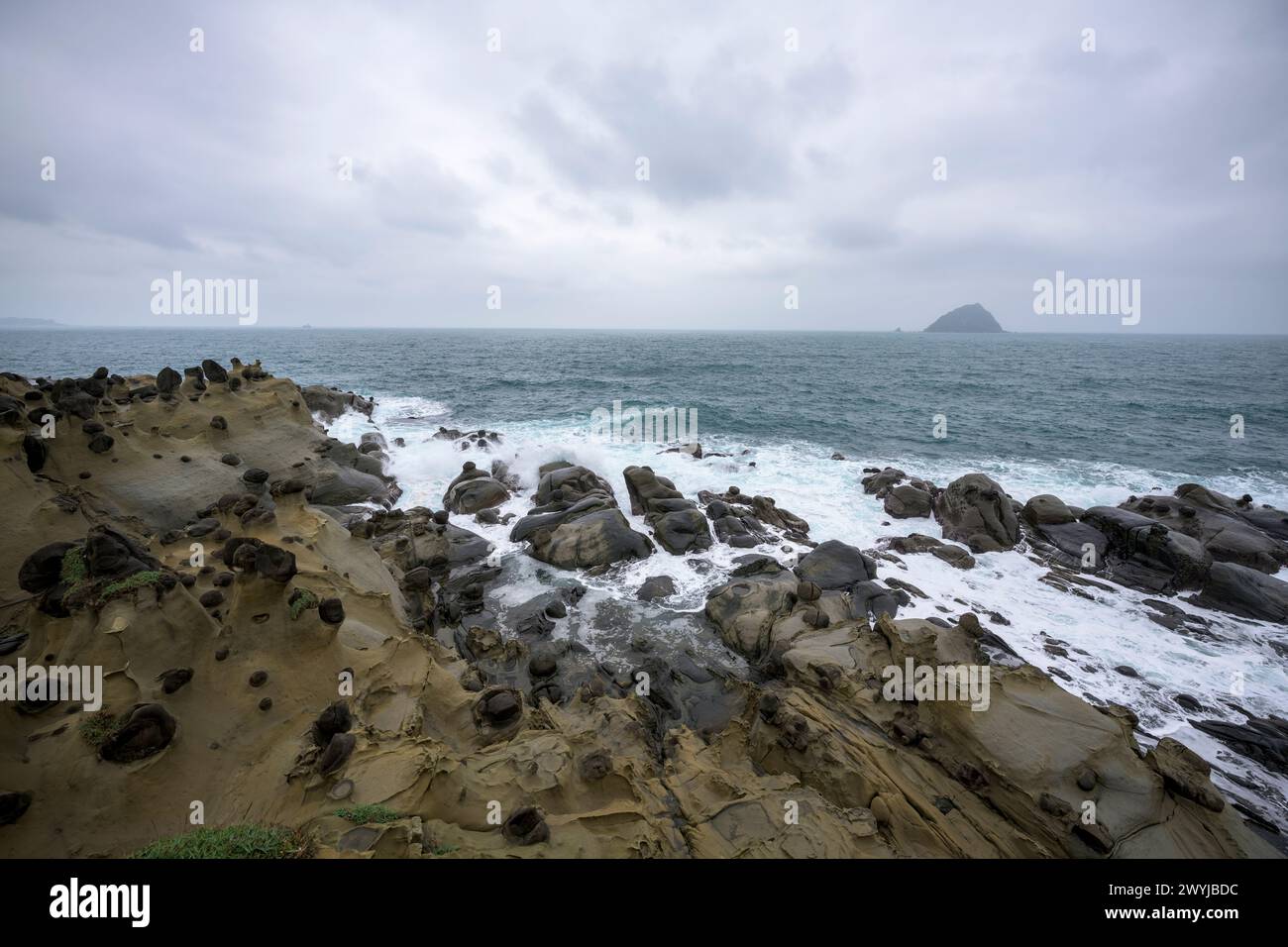 I cieli si snodano su una costa frastagliata con onde che si infrangono contro rocce erose in modo unico Foto Stock