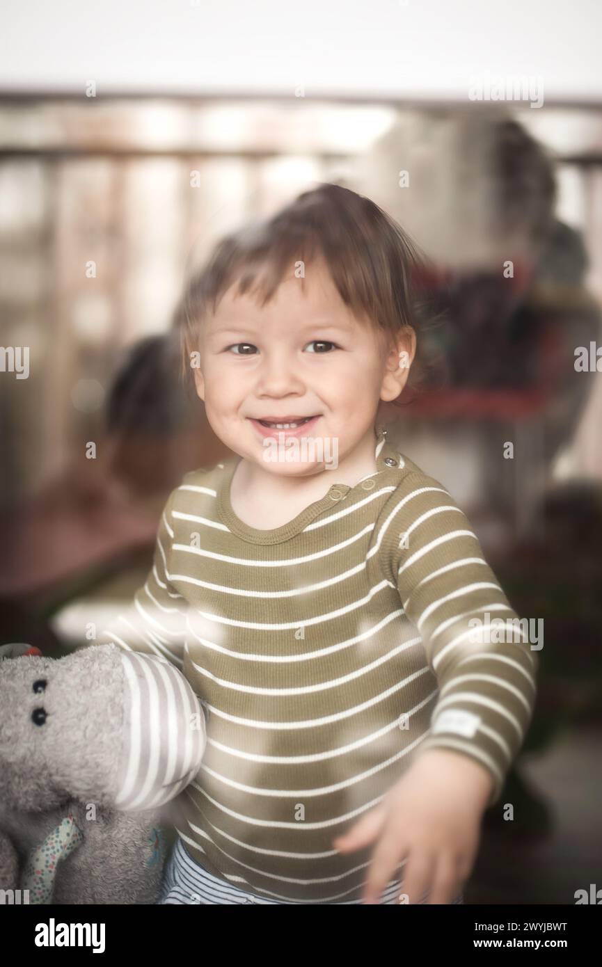 Un bambino allegro e felice guarda fuori dalla finestra dall'interno della camera. Vista dalla strada. Primo piano sorriso sulla faccia del figlio. Momento divertente Foto Stock