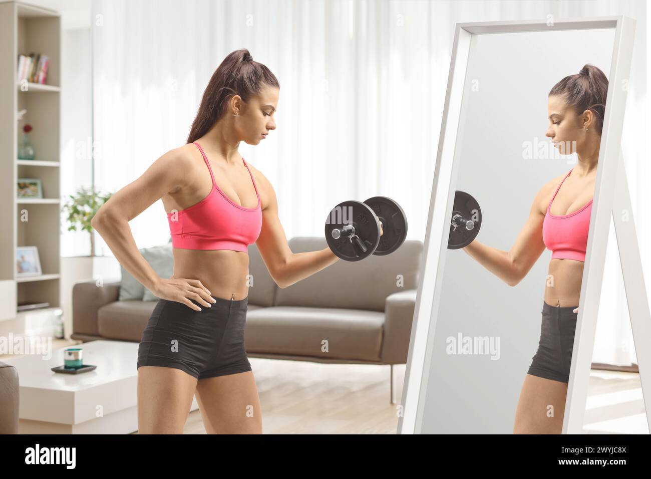 Adatta la giovane donna che fa esercizio con un manubrio davanti a uno specchio a casa Foto Stock