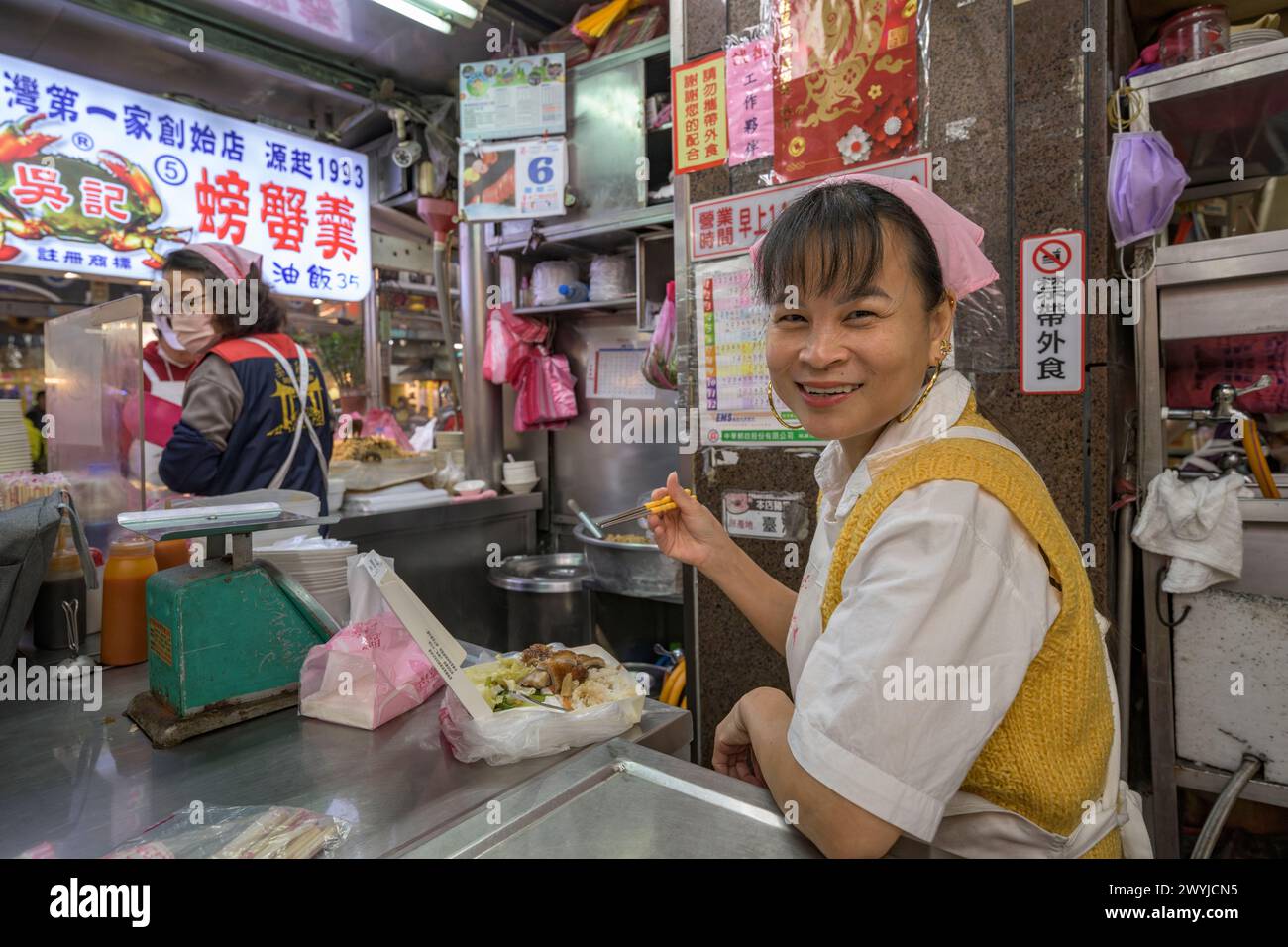 Una donna allegra si diverte a mangiare mentre lavora in un affollato mercato alimentare Foto Stock