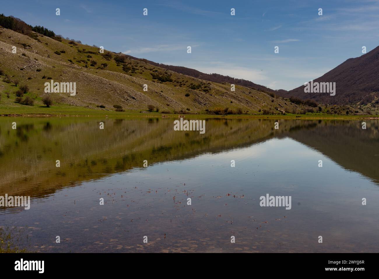 Un tranquillo lago di montagna riflette il cielo azzurro e le colline circostanti, creazione un'immagine speculare di pace e serenità Foto Stock