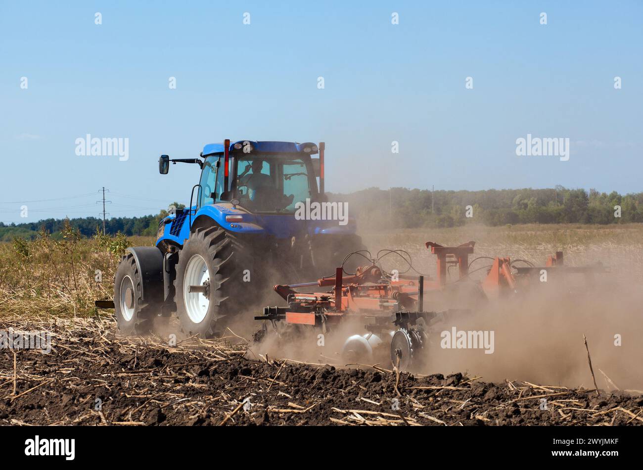 il trattore blu ara il campo e rimuove i residui di mais precedentemente tagliato. Parte del coltivatore, acciaio, dischi rotondi in una fila primo piano. agric di lavoro Foto Stock