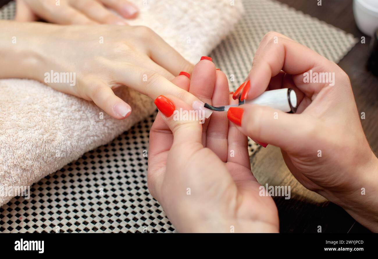 Il nail artist dipinge le unghie con smalto durante la procedura di estensione delle unghie con gel nel salone di bellezza. Cura professionale delle mani. Foto Stock